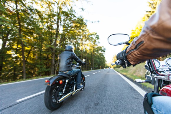 Two people riding motorcycles down a tree-lined road