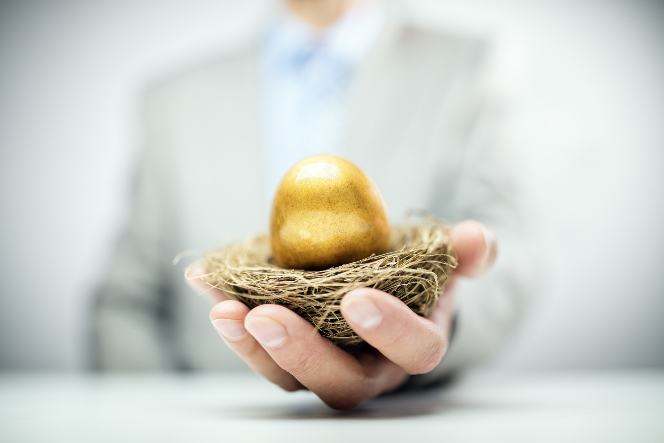 A man in a suit holding out a nest with a golden egg sitting in it