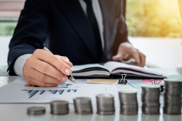 Business man pointing at charts with a pen, with growing stacks of coins in the foreground