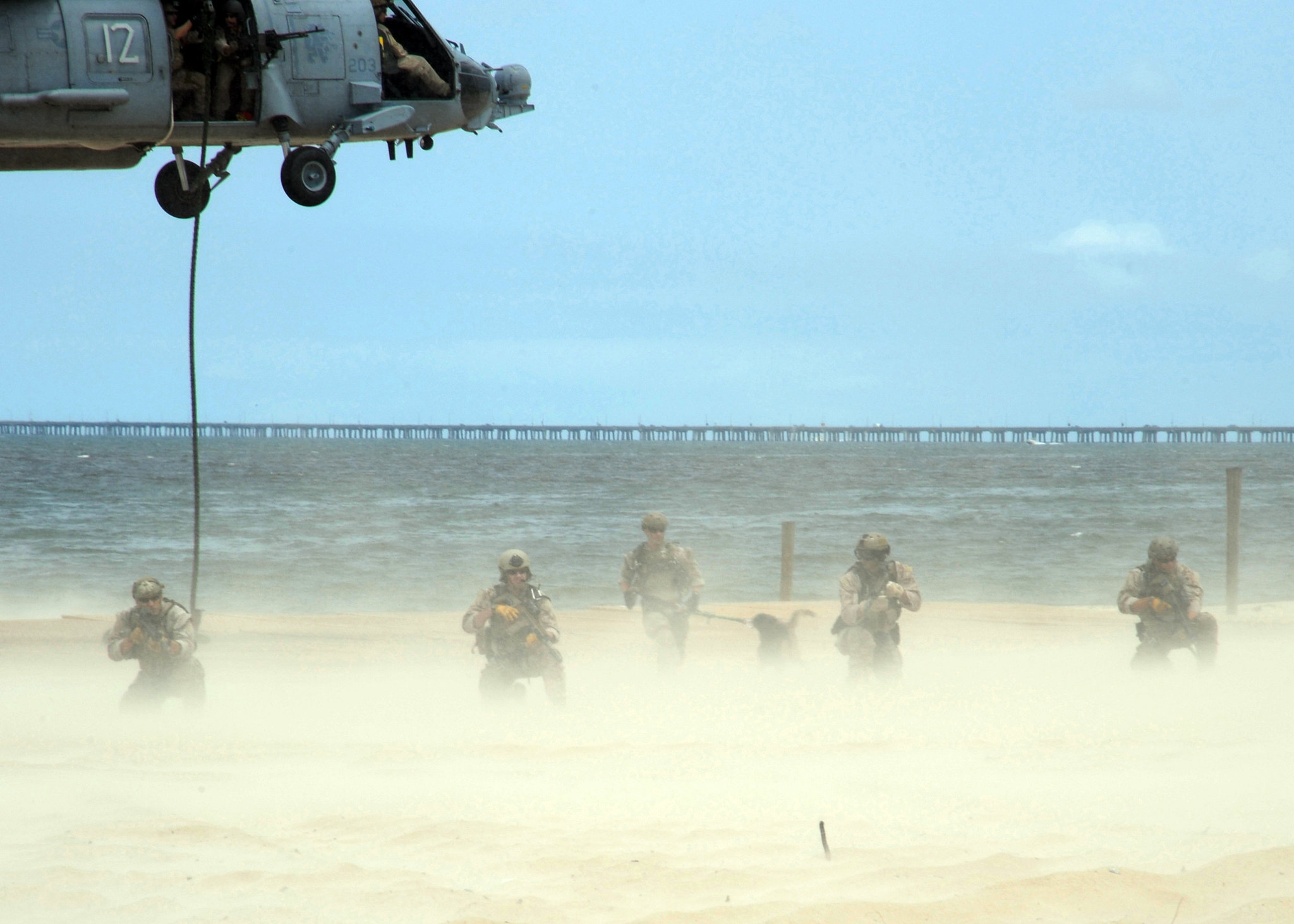 Five Navy seals landing on a beach with a helicopter overhead.