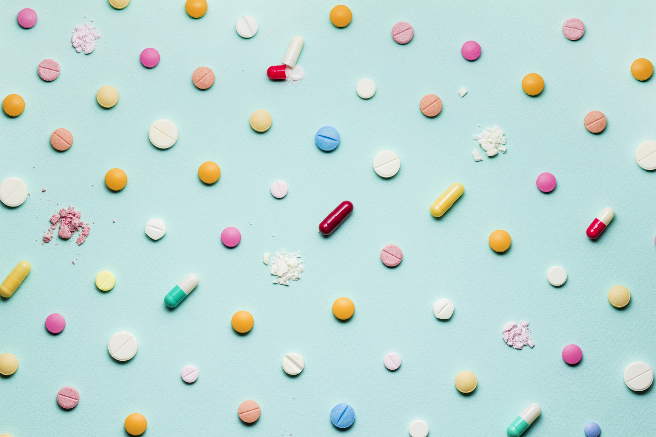 Many different capsules and pills, with some of the pills crushed, on a blue background