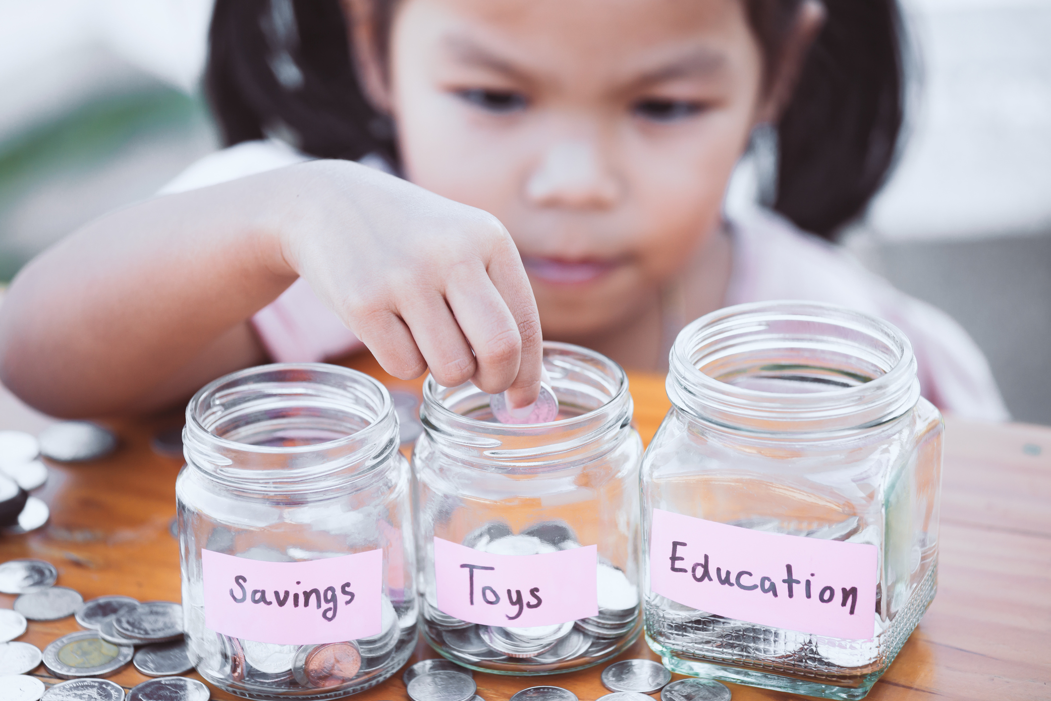 A child places coins in jars labelled "savings," "toys," and "education."