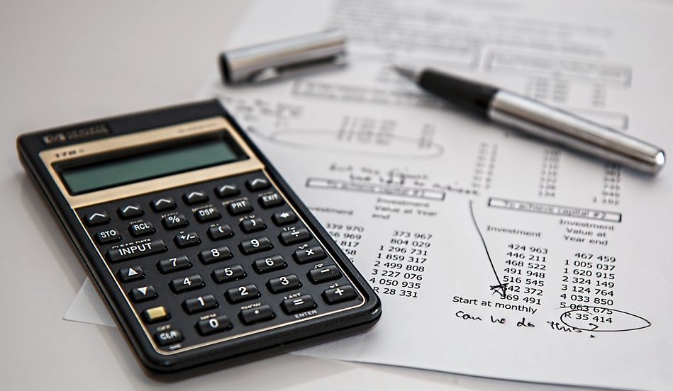 A calculator and pen sitting on paper that has numbers written on it.