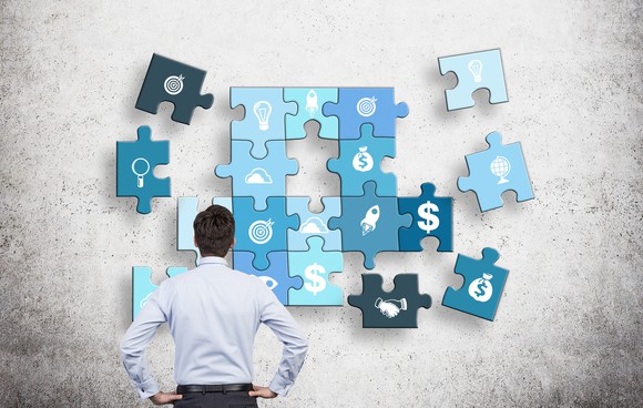 man with hands on hips looking at a puzzle of different business components on a concrete wall