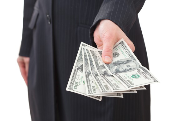 torso seen of man in suit, holding out hundred dollar bills