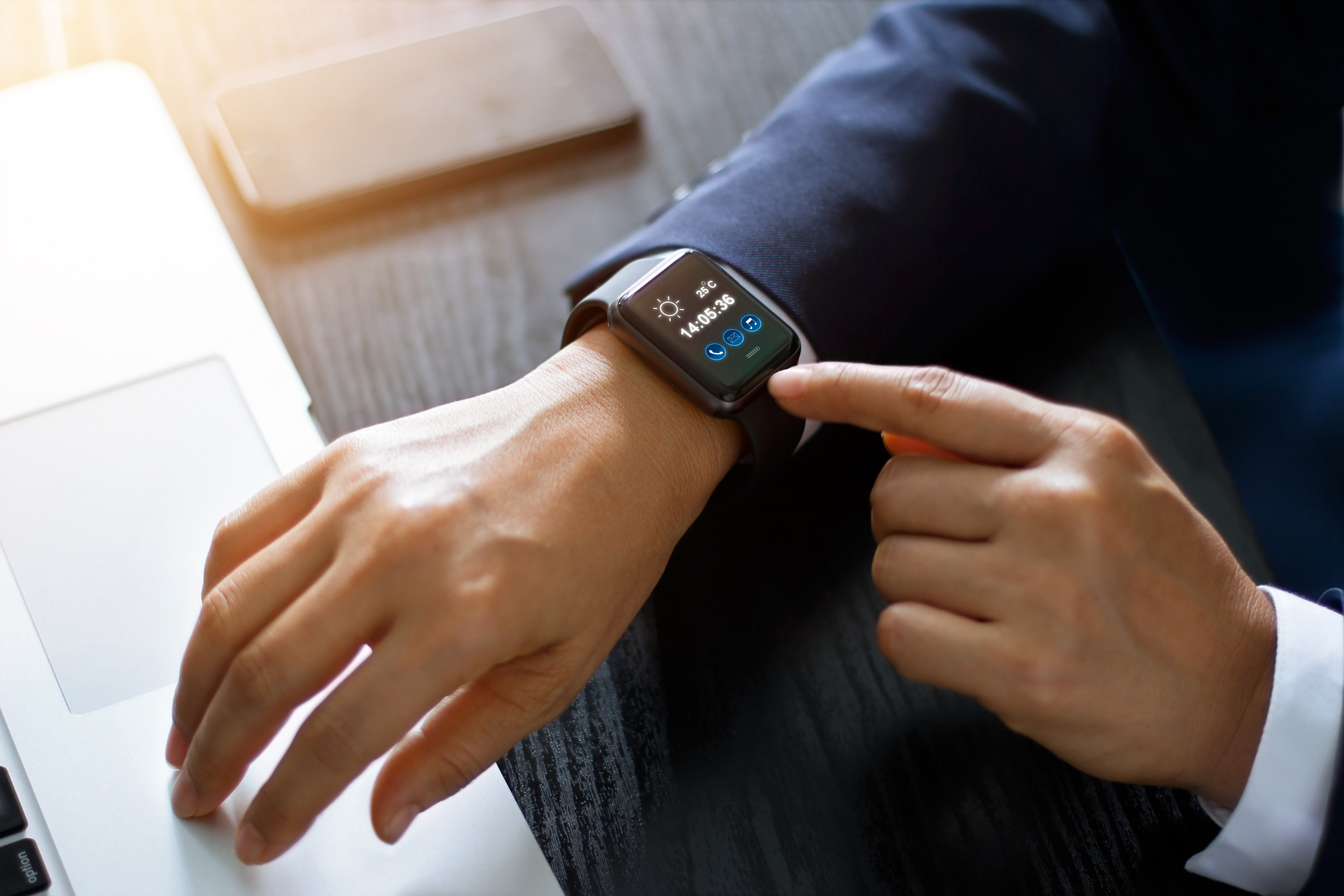 A person checks a smartwatch while using a laptop.