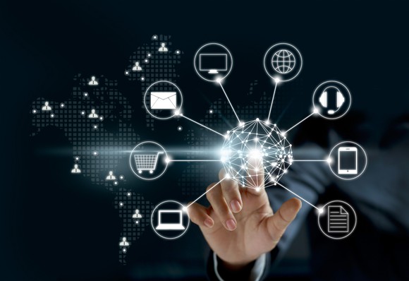 A hand touching a screen that has icons indicating various technologies, like computers, email, and online shopping.