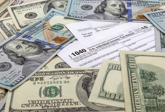 100 dollar bills scattered on a 1040 tax form.