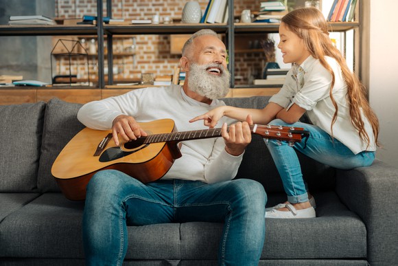 Grandfather chatting with granddaughter while holding a guitar.