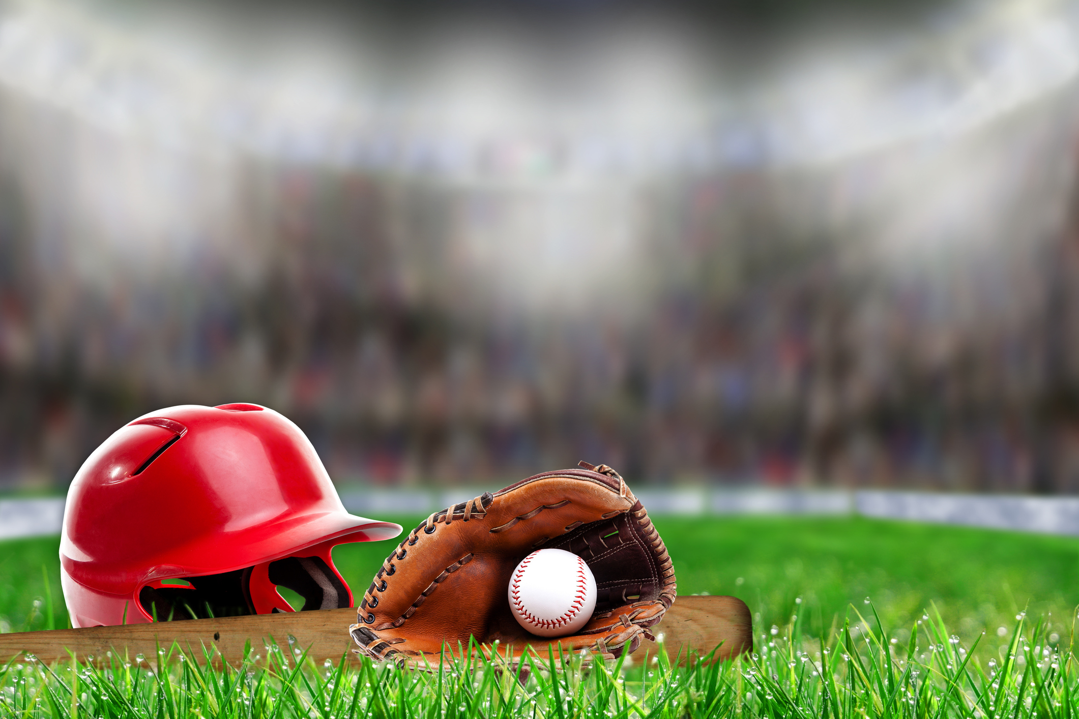 A baseball helmet, glove, ball, and bat on the field in a stadium.