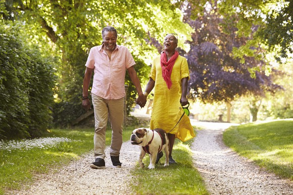 Two retirees walking their dog in a park.