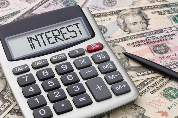 Calculator displaying word "interest" sitting atop dollar bills
