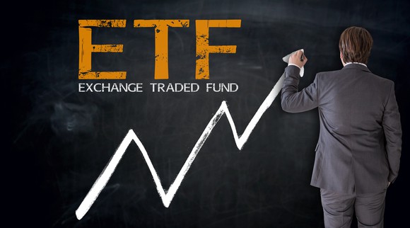 The letters ETF and Exchange Traded Fund on a blackboard, with a man in business suit drawing an arrow going up.
