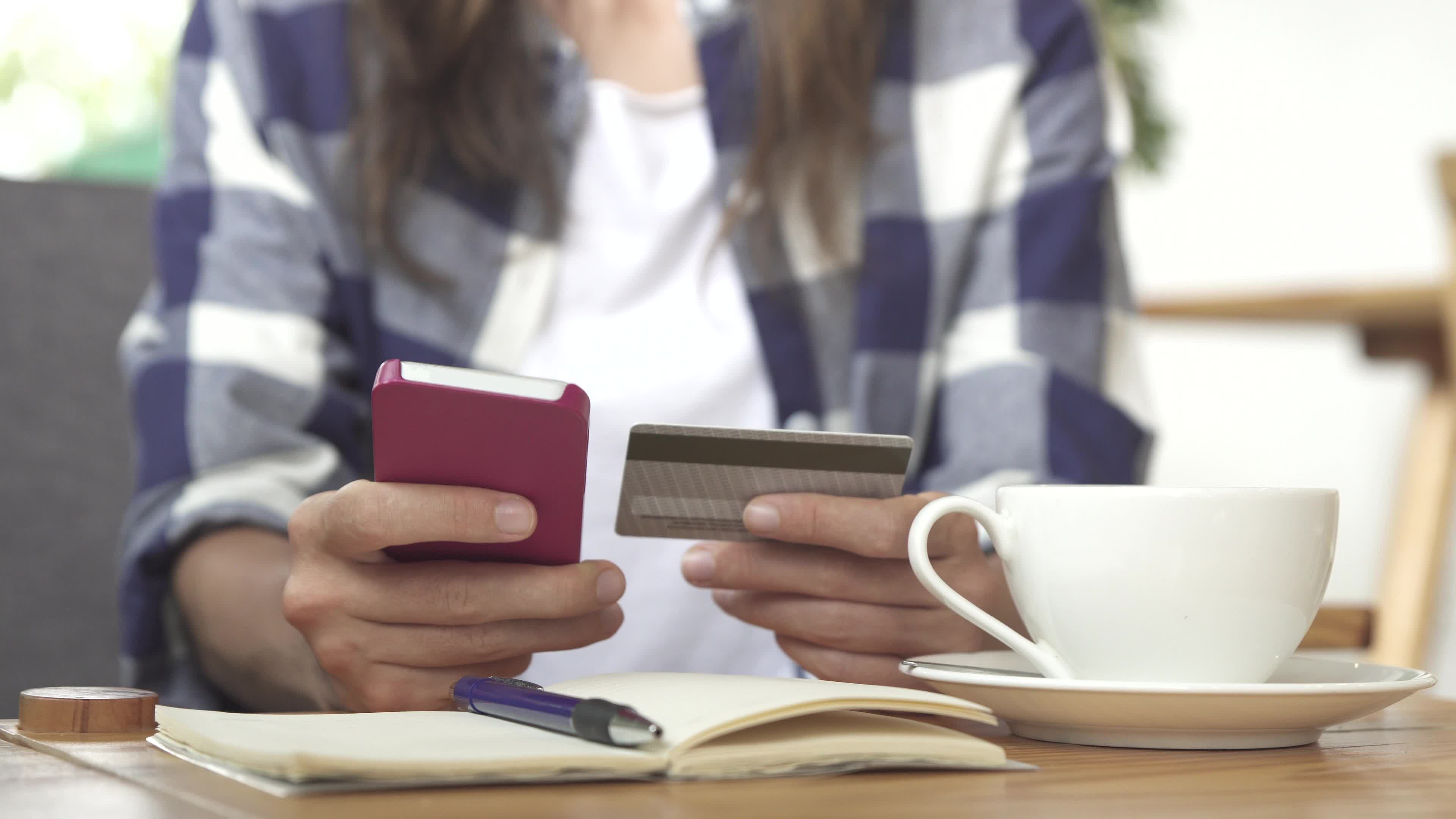 A woman holds a smartphone in one hand and a credit card in the other.