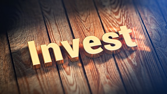 The word "Invest" written in gold sitting atop wooden boards.