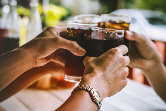 Four hands holding glasses of soda and clinking them together