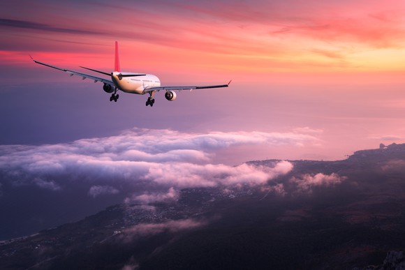 A plane flying high over a city against a pink and yellow sky.