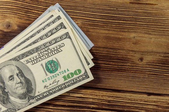 A stack of $100 bills on a wooden table.