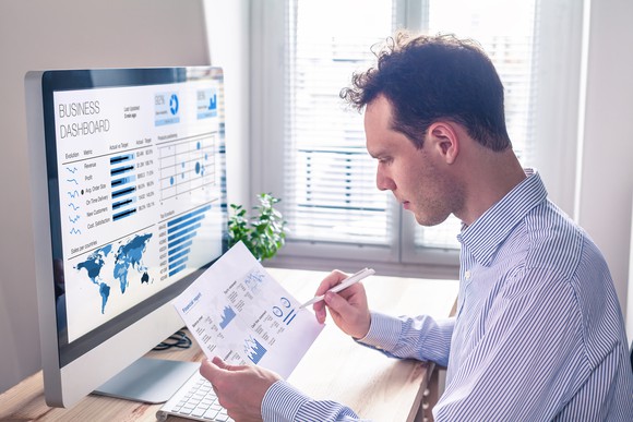 An investor checks a printout of stock information against charts on his computer screen.