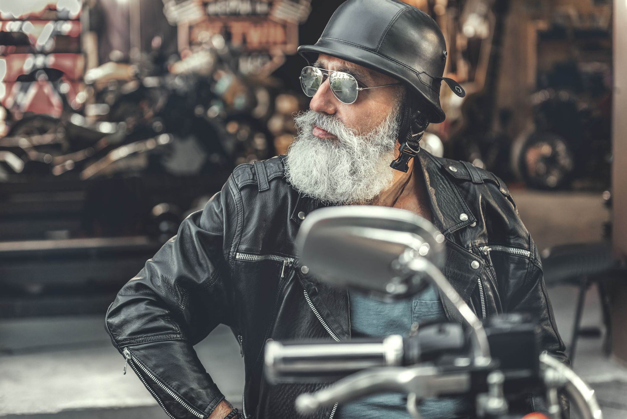Grey-bearded man wearing sunglasses and helmet astride a motorcycle