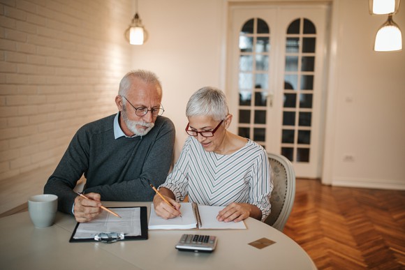 Married couple sitting at a table with papers and a calculator and discussing retirement.