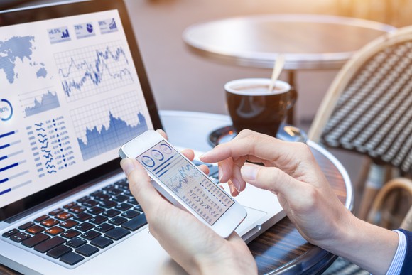 Man checking stock charts on laptop and smartphone.