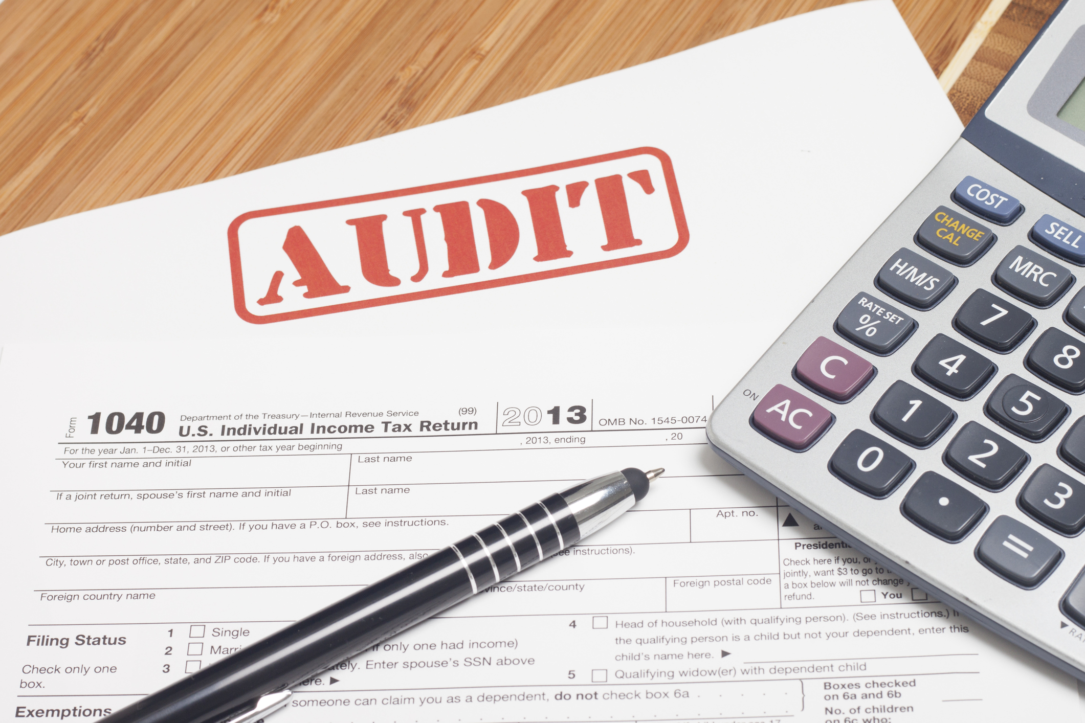Red audit stamp on tax paperwork with pen and calculator nearby.