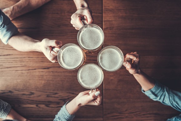 Overhead view of four people's arms toasting with beer steins