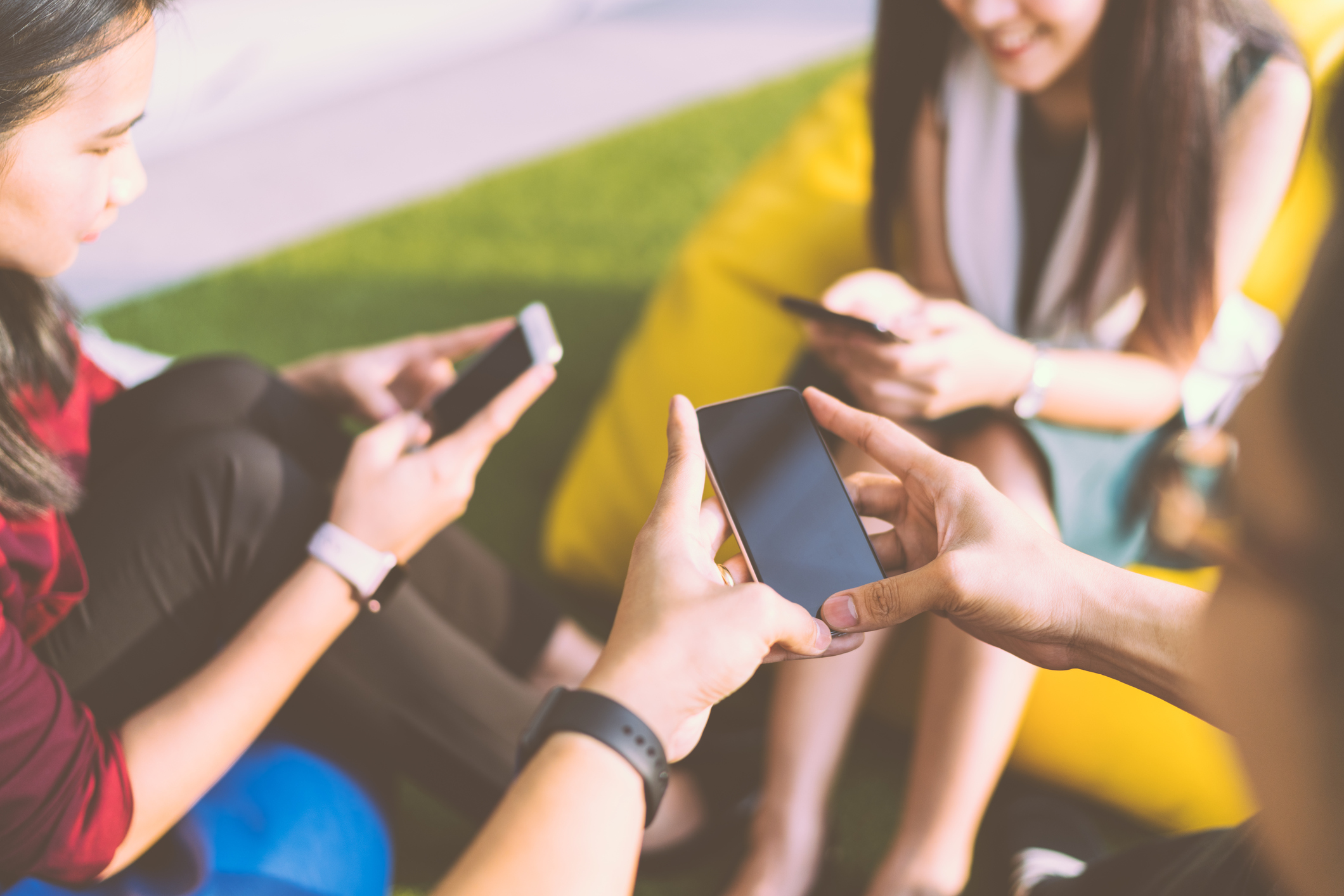 Several teenagers sitting a circle and looking at their mobile phone screens