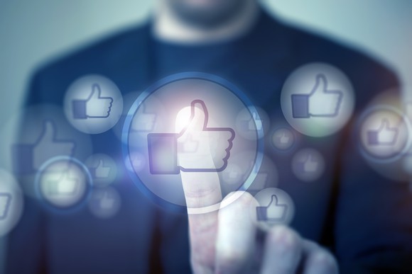 A man pressing Facebook's thumbs-up "like" symbol.