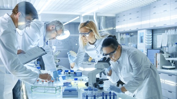 Four professionals in white coats working in a lab.