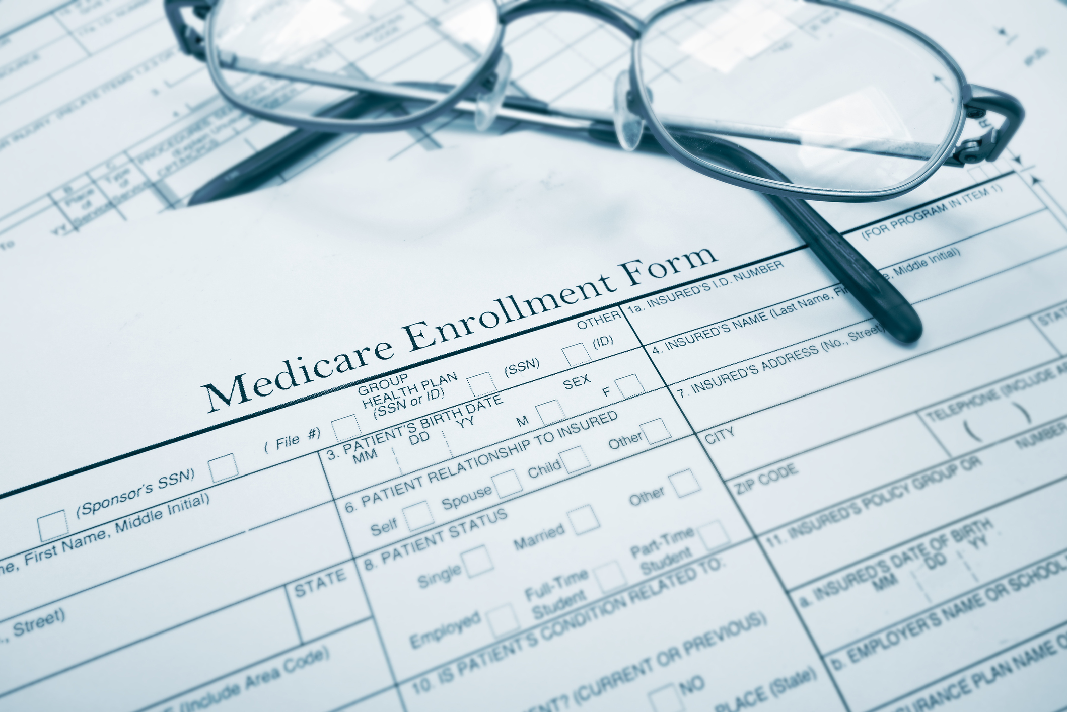 A pair of reading glasses rests on top of a Medicare enrollment form.