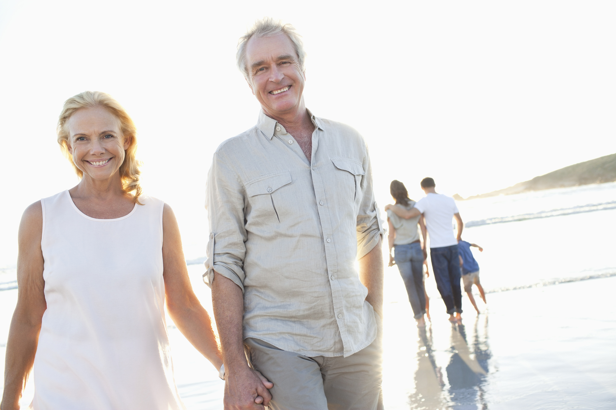 Male and female couple in their 60s walking on the beach.