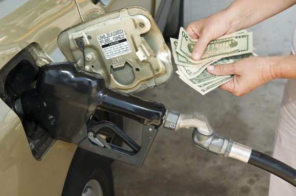 Someone counts money while a gas pump fills a car with gas.