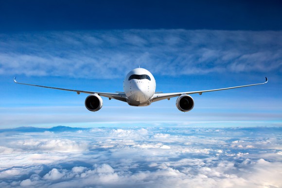 A plane flying straight on above the clouds