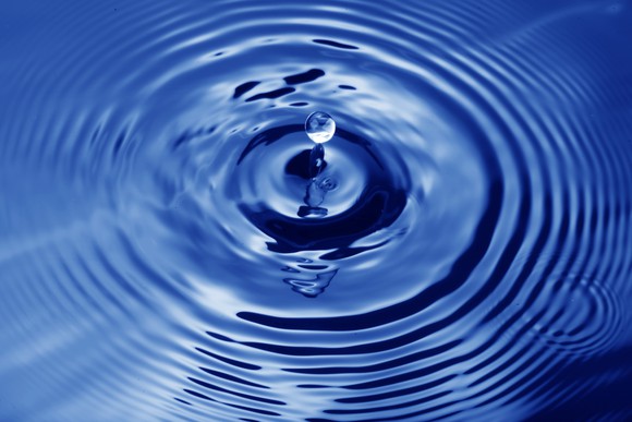 A drop of water falling into a body of water, with ripples emanating from it.