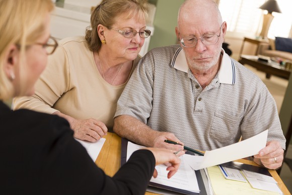 Senior Couple Discussing Paperwork With Advisor Getty