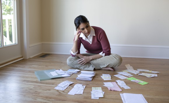 Woman with a worried look sitting on the floor, looking through piles of receipts.
