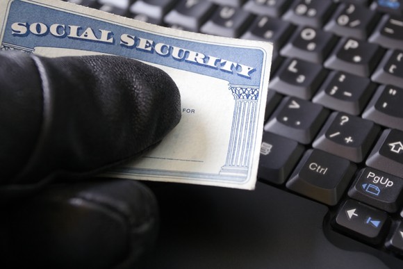 hand in black glove suspiciously holding Social Security card by keyboard