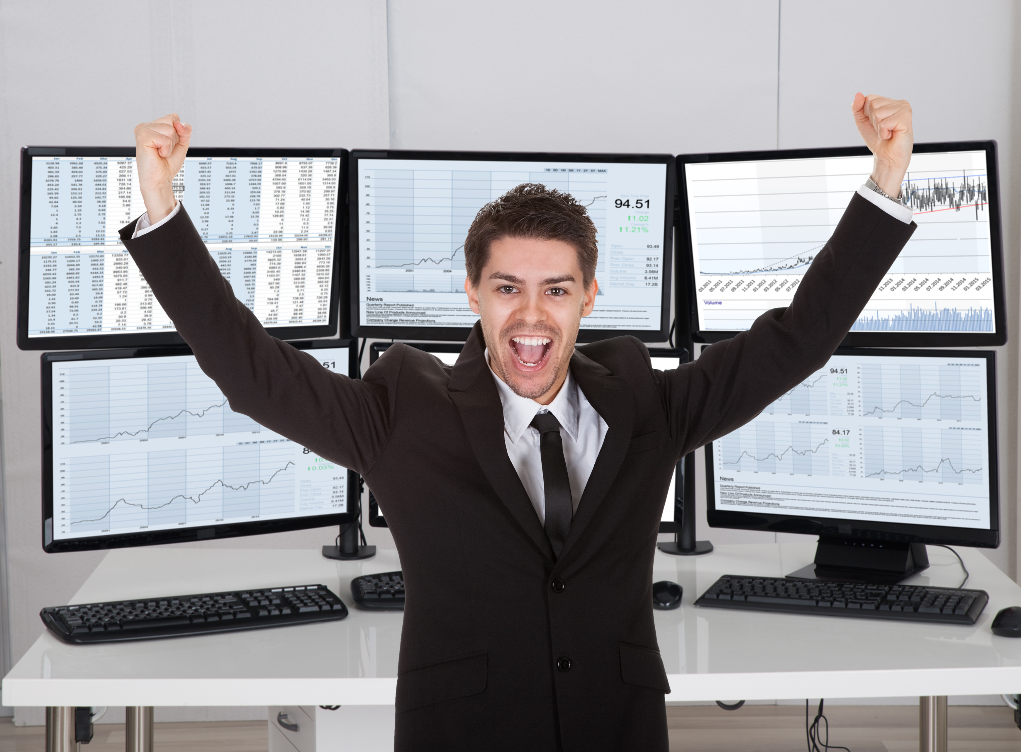 Stock broker celebrating in front of multiple computer screens.