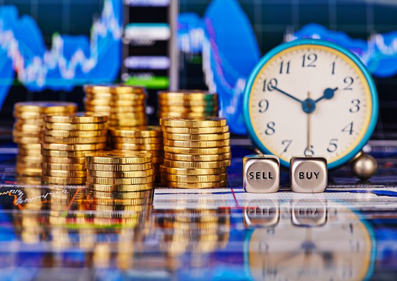 Stacks of gold coins with a clock and a pair of dice which say "buy" and "sell"