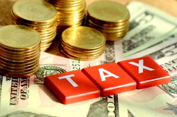 Gold coins and tiles spelling "Tax" on top of a pile of money.