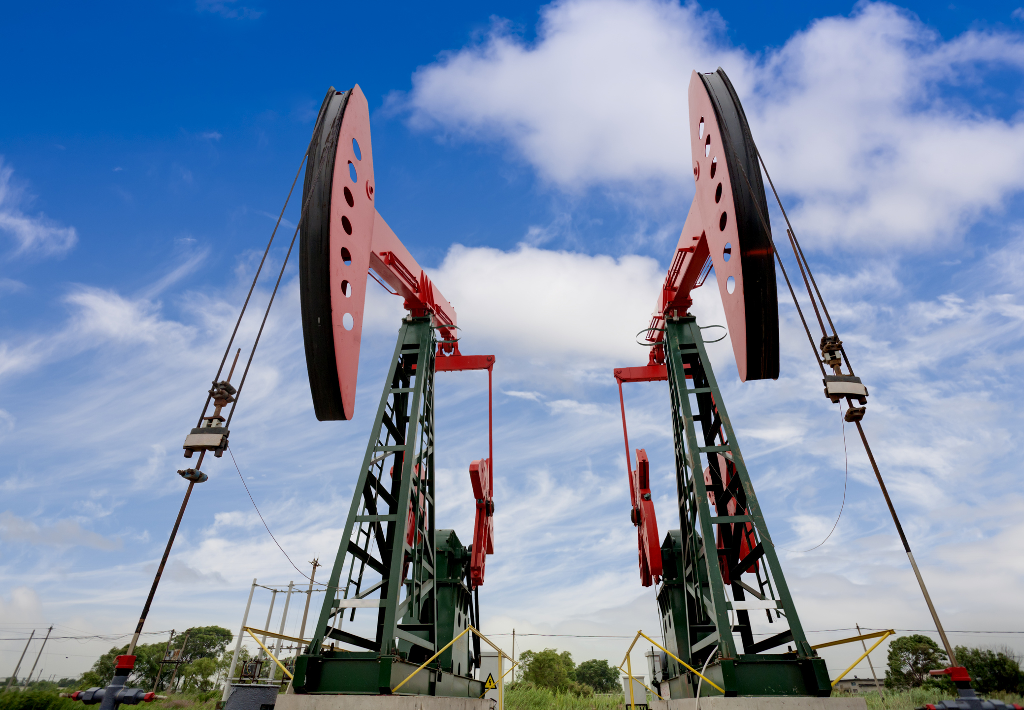 Two oil wells side-by-side with a blue sky in the background.