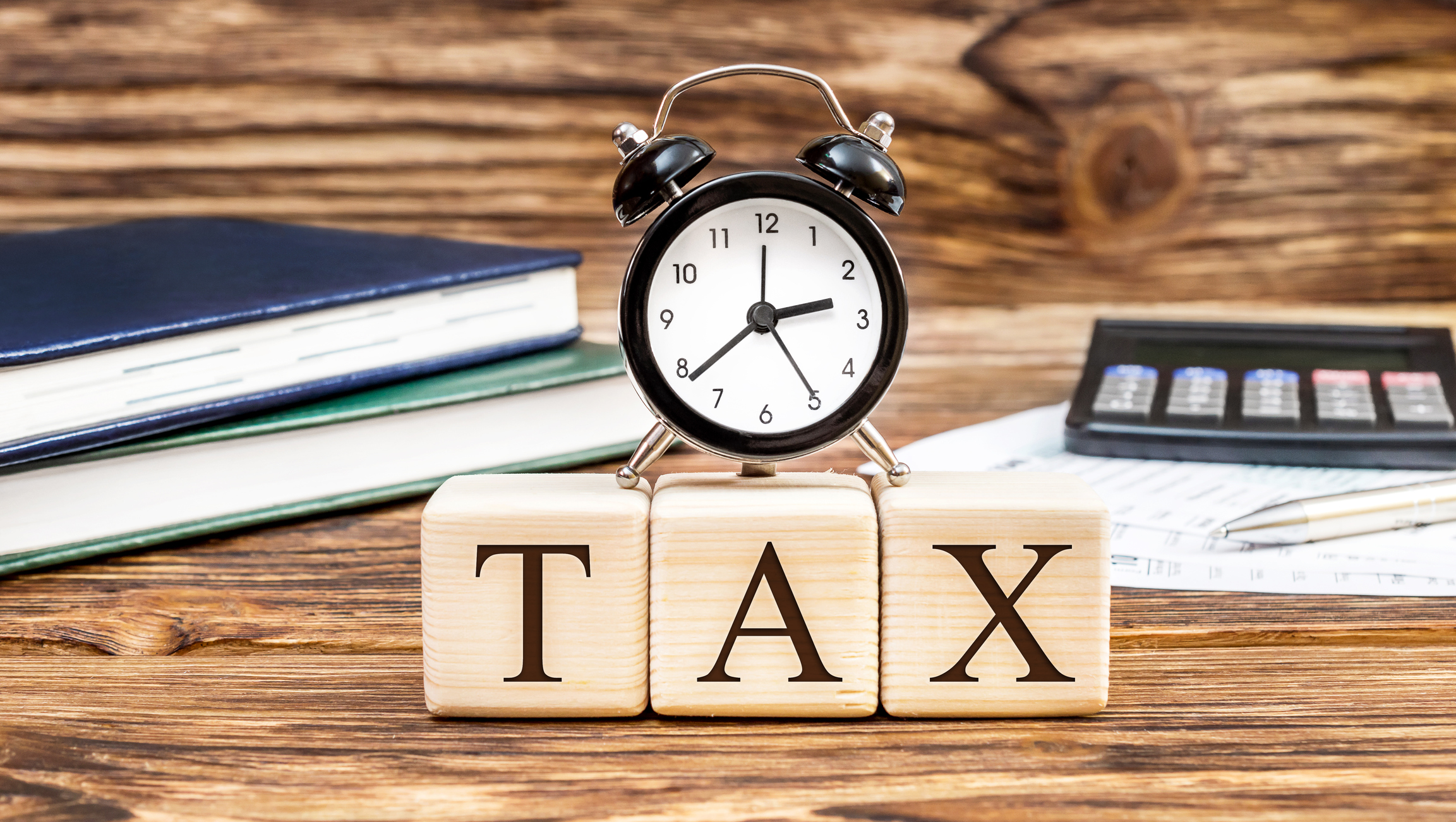 An alarm clock sits atop wooden blocks that spell out "TAX."
