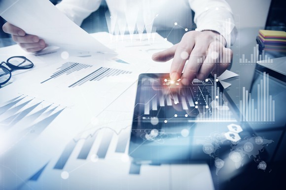 An investor looks over a paper and tablet with financial results.