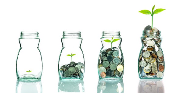 Four glass jars, each filled progressively higher with coins and a green sprout.
