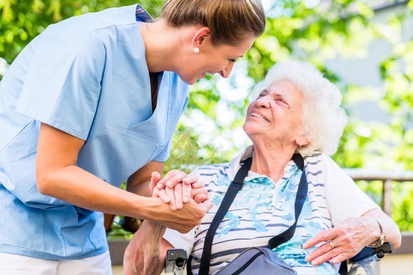 Younger woman in scrubs tending to older woman in wheelchair
