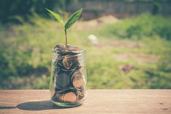 A green sprout coming out of a glass jar full of coins.