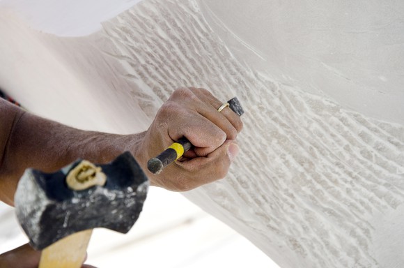 Hands holding a hammer and chisel to sculpt.