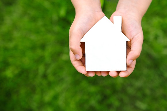 Two hands holding a little paper house.